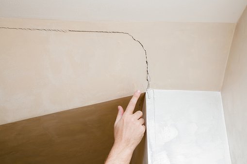 istockphoto-987519662-170667a Man's hand finger pointing to the cracked wall in house. Building problems and solutions concept.